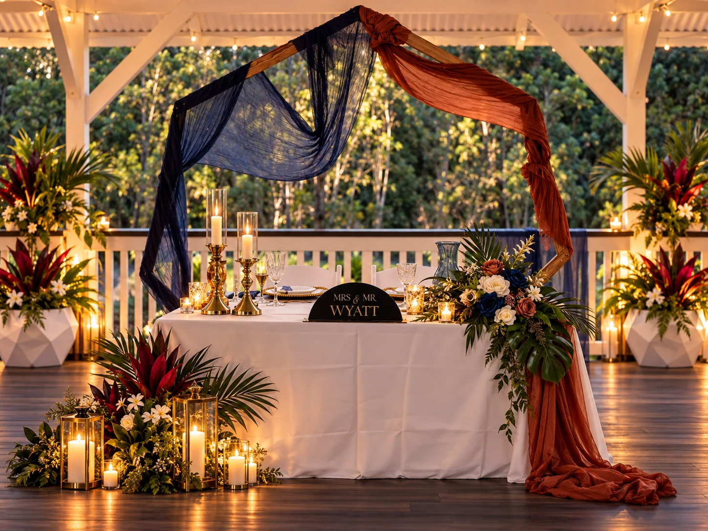Sweetheart table with navy and rust draping, candles and tropical florals